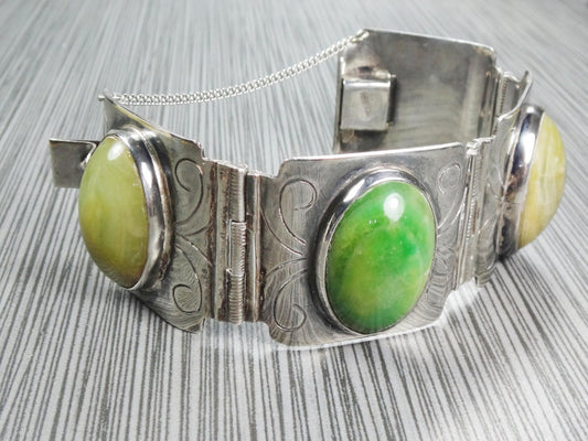 Vintage Wide Sterling Silver Green Stone Bracelet Made in Mexico. A silver bracelet with oval shaped green stones. The bracelet has a hinged clasp and is decorated with an engraved swirl pattern.