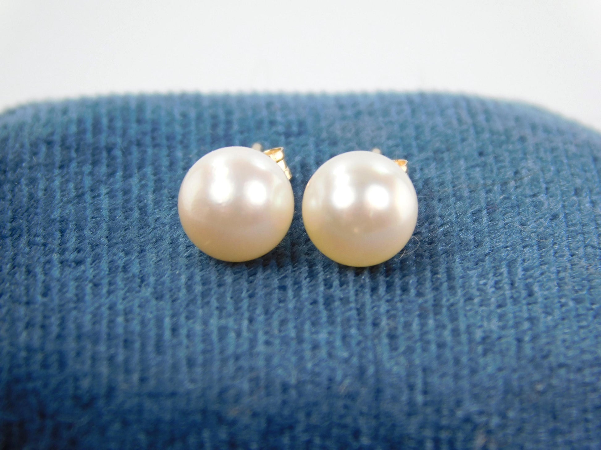 A close up of a pair of white cultured pearl stud earrings from the front. The yellow gold posts and backs aren't shown as much as the pearls themselves.  These are classic pearl studs.