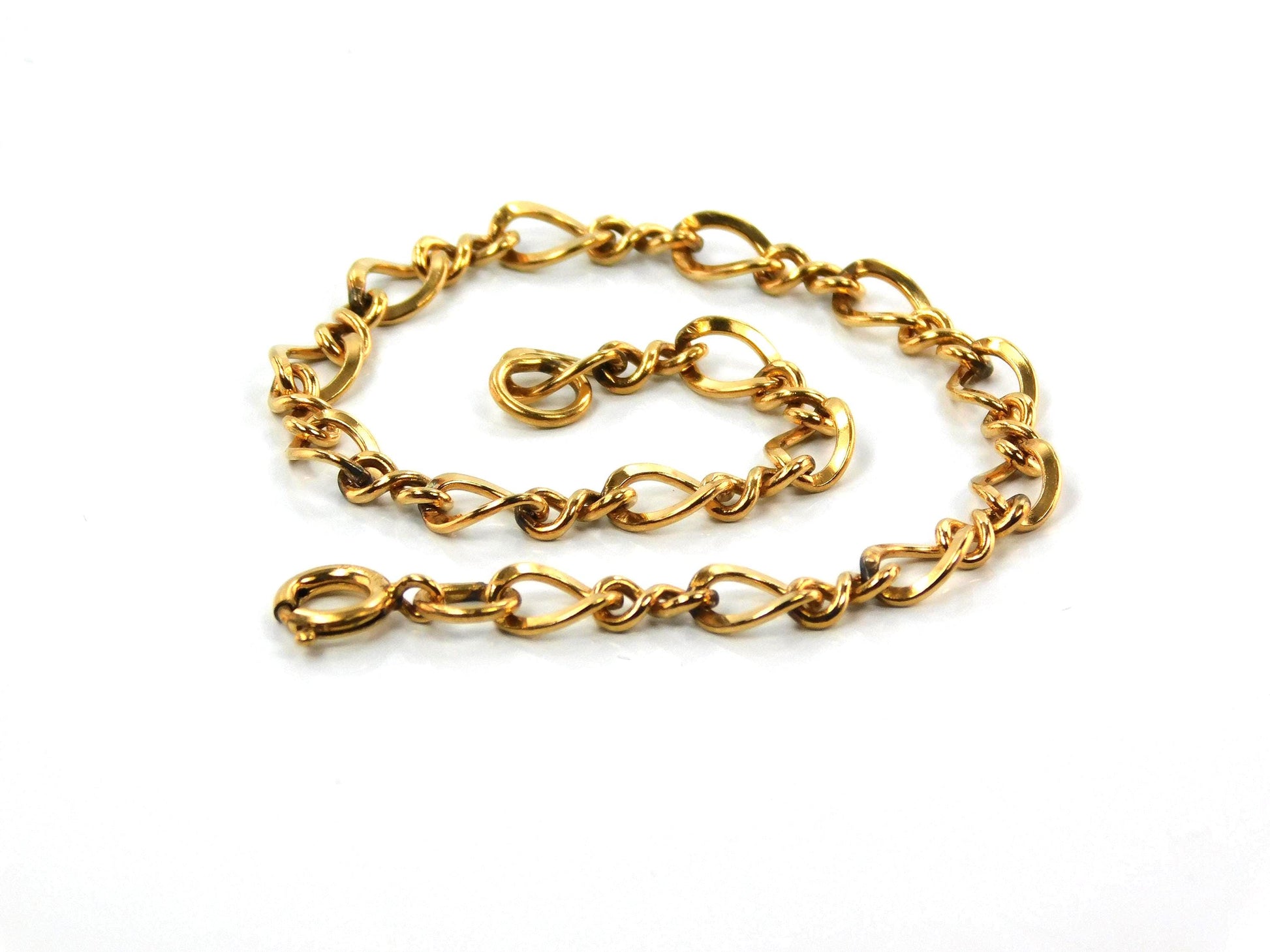 A close up of a vintage 14k yellow gold filled link bracelet with a spring clasp. The links shaped like number eight and plain links are interspersed with each other.