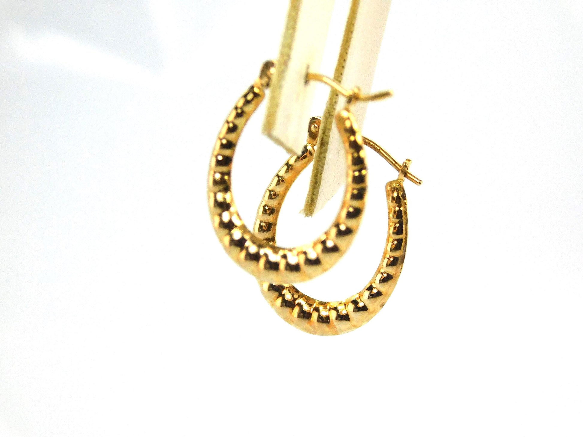 A close up of a pair of 14k yellow gold hoop earrings with an oval shape, ribbed design and polished finish.
