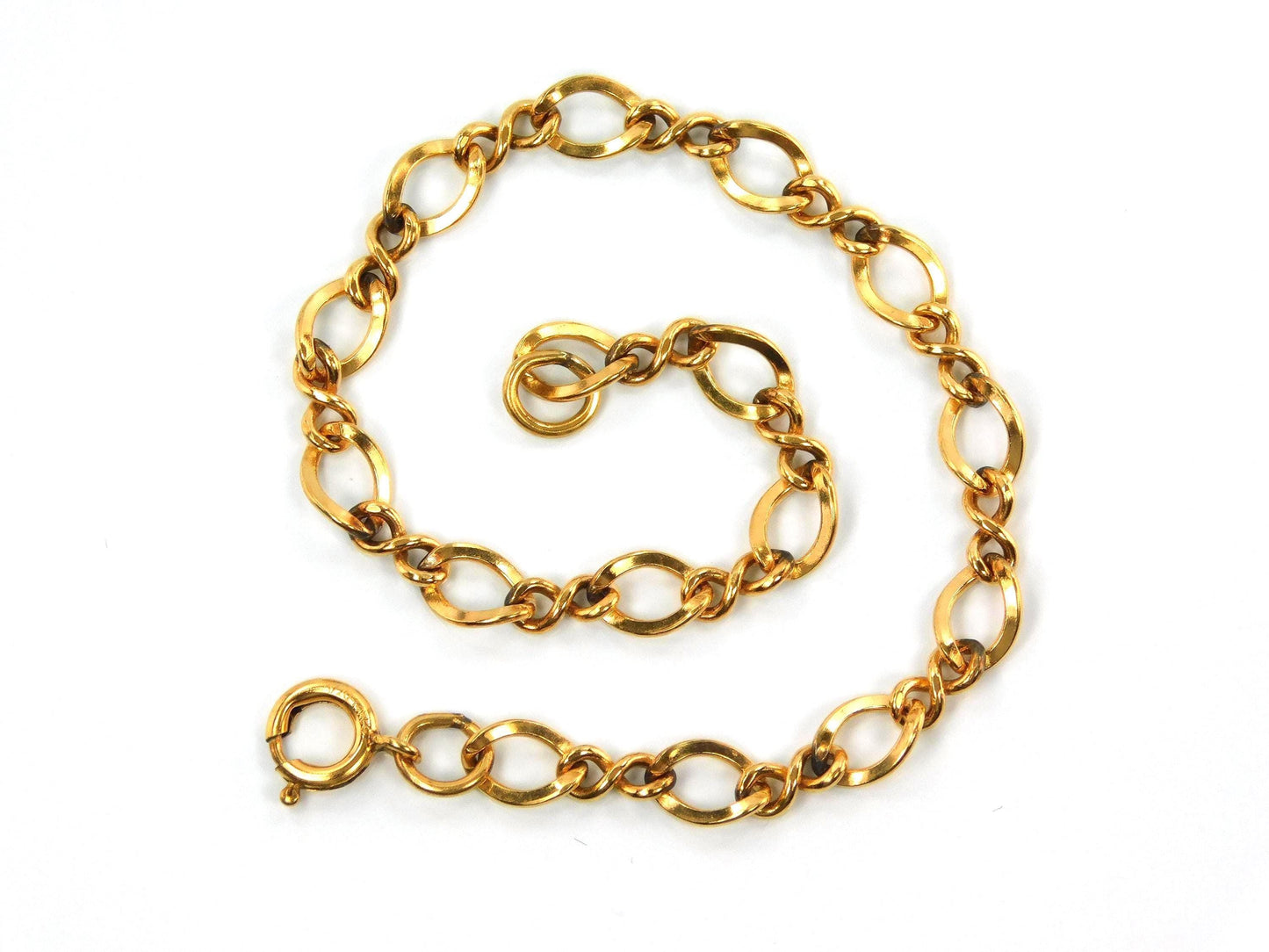 A close up of a vintage 14k yellow gold filled link bracelet with a spring clasp. The links are all slightly twisted and shaped like number eights mixed with oval links.