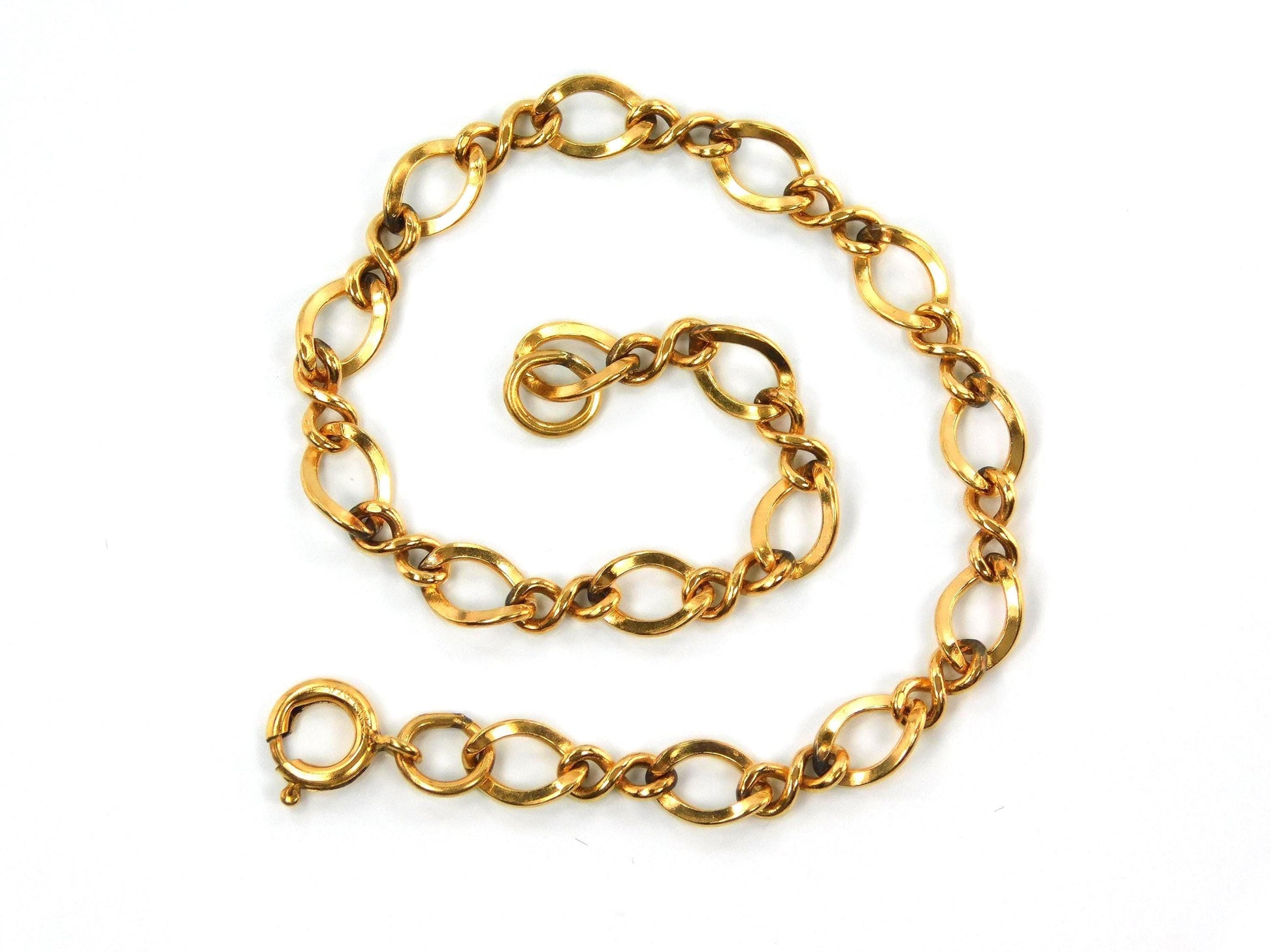 A close up of a vintage 14k yellow gold filled link bracelet with a spring clasp. The links are all slightly twisted and shaped like number eights mixed with oval links.
